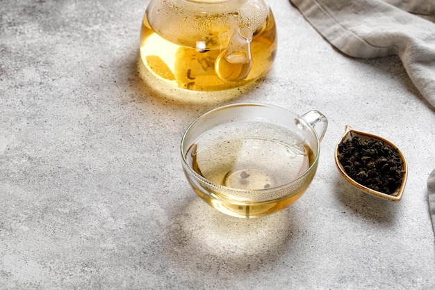 A mug or cup with green herbal tea and a teapot with tea leaves on grey background. Beauty color