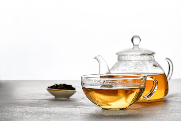 A mug or cup with green herbal tea and a teapot with tea leaves on grey background. Beauty color