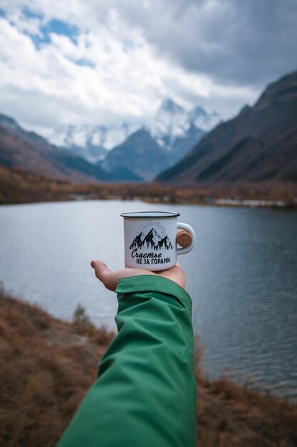 Photo mug in hand against the background of a beautiful mountain lake