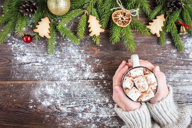 Mug of hot chocolate with marshmallow, spices, Christmas ginger cookies, fir branches and cones on dark wooden background. Copy space for text. Christmas wallpaper, card.