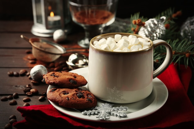 Mug of hot chocolate with marshmallows, fir tree branch on wooden surface