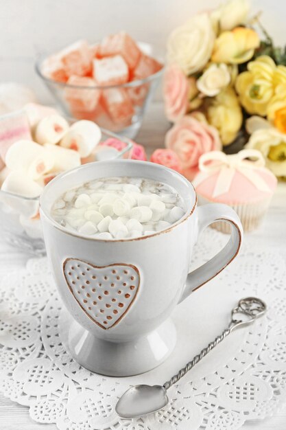 Mug of hot chocolate with marshmallows on light wooden background