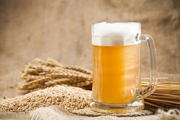 Mug of light beer with pile of wheat an sackcloth background