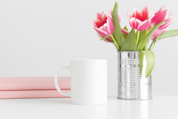 Mug mockup with pink tulips in a pot and books on a white table