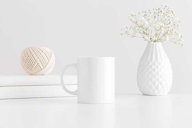 Mug mockup with workspace accessories and a gypsophila on a white table