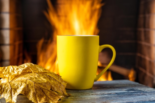 Mug for tea or coffee and autumn leaves before cozy fireplace