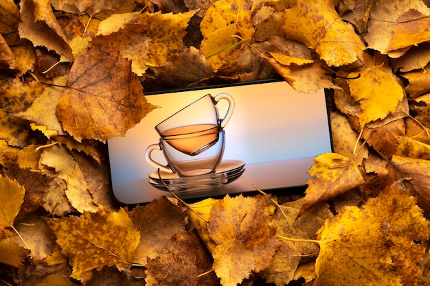 A mug of tea on the mobile phone screen against the background of autumn leaves orange cocept herbal tea tea party or healthy lifestyle concept tea card