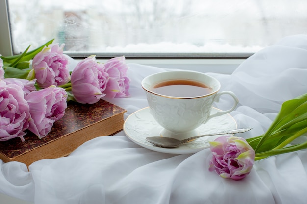 お茶のマグカップ古い本窓にチューリップの花束