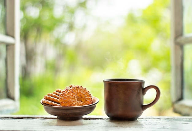 夏に開いた窓の窓辺にお茶のマグカップとクッキーのプレートが立っています