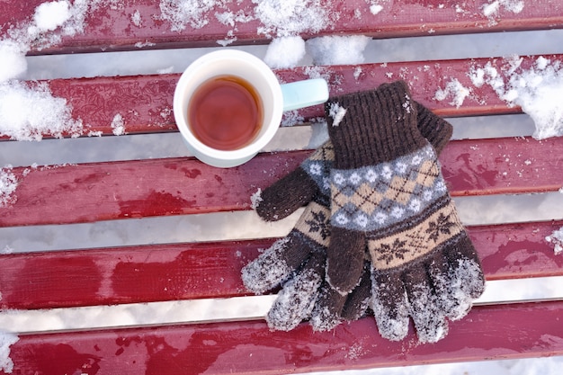 Photo mug of tea and women's knitted gloves on a bench