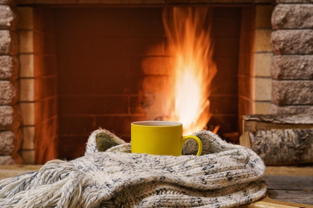 Una tazza di tè e una cosa di lana vicino a un accogliente caminetto in una casa di campagna durante le vacanze invernali o autunnali