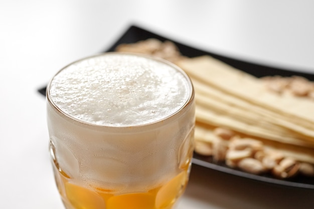 Mug of unfiltered light wheat beer with beer snacks on white table