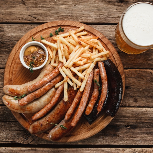 Mug with beer and delicious grilled sausages and french fries served with delicious sauce, closeup view. 
