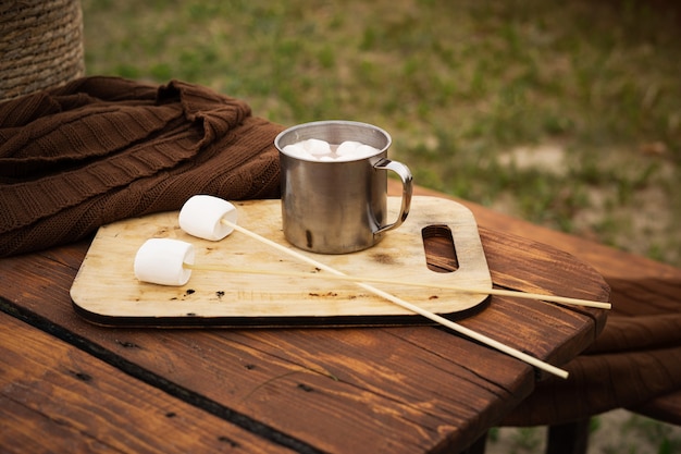 Mug with cocoa and marshmallows on sticks on wooden table