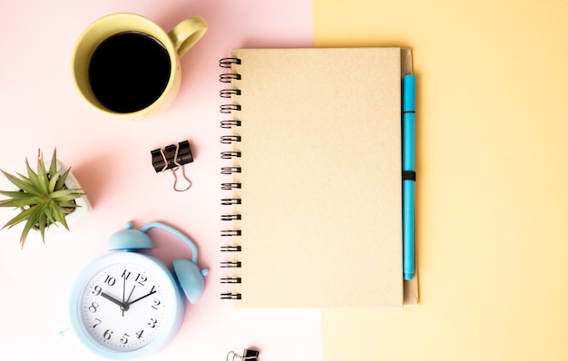 Mug with coffee, flower, alarm clock and paper notepad Premium Psd on a pink and yellow table.