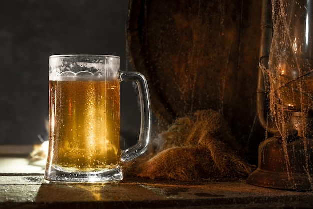 Mug with fresh light beer with foam on wooden vintage background with barrelÑ Old wine cellar or pub