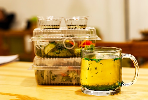 Tazza con brodo caldo ed erbe su un tavolo di legno e cibo da asporto a distanza sociale