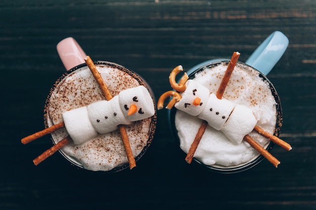 A mug with hot chocolate on a wooden table with a marshmallow man who is resting in a mug