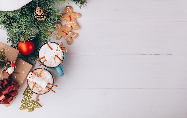 A mug with hot chocolate on a wooden table with a marshmallow man who is resting in a mug