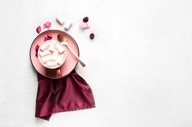 Mug with hot coffee and marshmallows on a pink plate on a gray surface