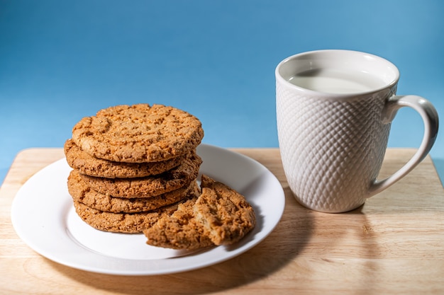 A mug with milk and oatmeal cookies on a wooden table white plate with fresh oatmeal cookies on a bl...