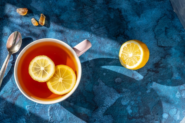 A mug with tea and lemon slices floating in it on a blue background