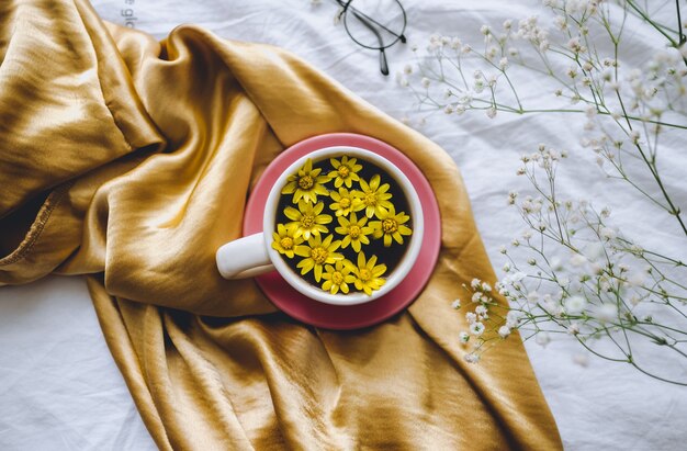 Mug with yellow flowers inside, on a golden satin fabric