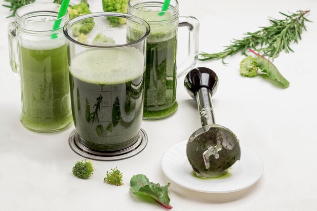 Coppe con frullato di verdure verdi chopper di metallo sul piatto raggi di rosmarino e broccoli sul tavolo