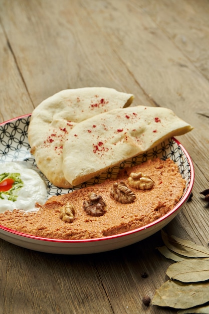 Muhammara is a classic eastren dish. baked pepper and walnut puree with Bazlama and yogurt in a ceramic plate on a wooden surface.