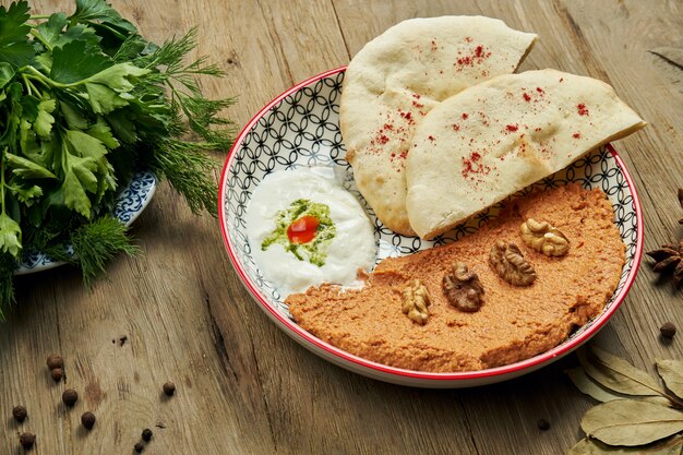 Muhammara è un classico piatto eastren. purea di pepe e noci al forno con bazlama e yogurt in un piatto di ceramica su una superficie di legno.