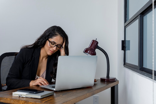 Photo mujer aburrida revisando sus mensajes de celular mientras trabaja desde casa por la cuarentena