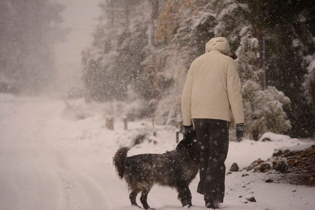 mujer caminando en la nieve con tormenda y perro que la acompana