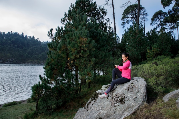 Photo mujer corredora usando su reloj inteligente despues de correr sentada en la orilla del lago