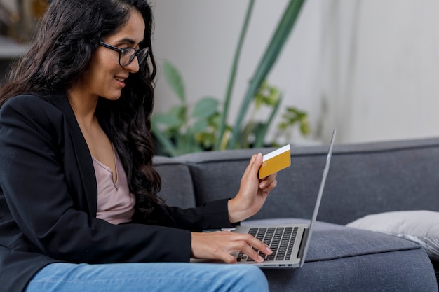 Mujer latina comprando en line desde su casa en su Laptop y pagando con su tarjeta de credito