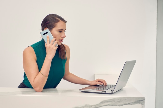 Mujer latina hablando por telefono mientras trabaja en su laptop