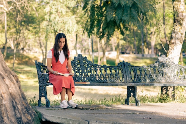 Photo mujer latina sentada en una banca de un parque leyendo un libro