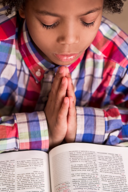 Foto mulat jongen bidden. kid in shirt is aan het bidden. jonge man met gebedenboek. zijn geloof is sterk.