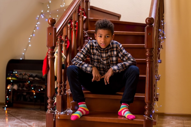 Mulatto boy in colorful socks young boy sits on staircase when holidays come near few hours before c...