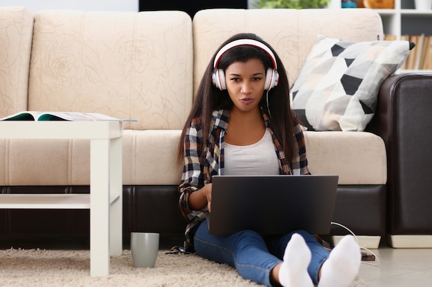 Mulatto girl in headphones at home on floor with laptop