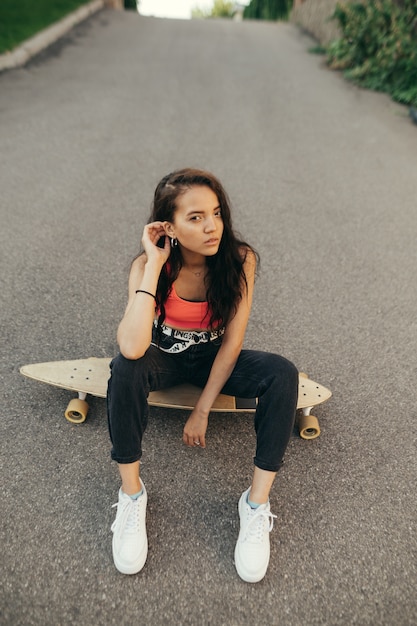 La ragazza mulatta si siede sullo skateboard