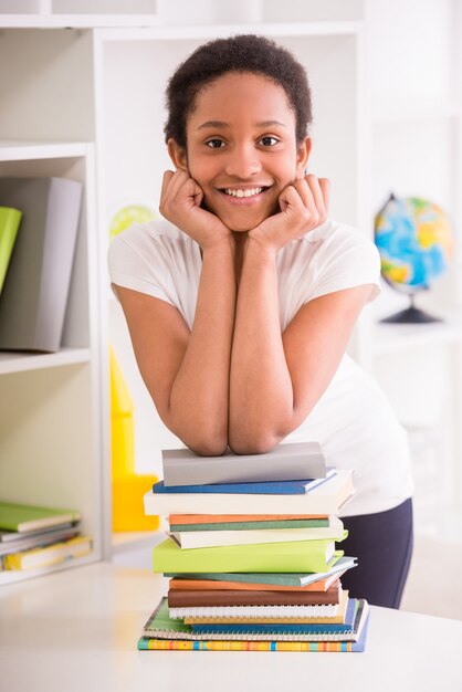 Mulatto schoolgirl standing with stack of books.