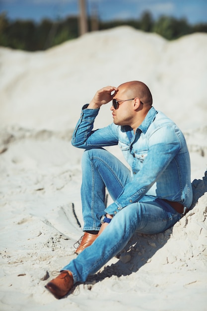 Mulatto tanned sitting on the sand in glasses