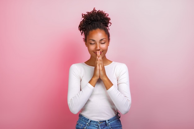 mulatto woman in supplication pose with smile and close eyes over pink