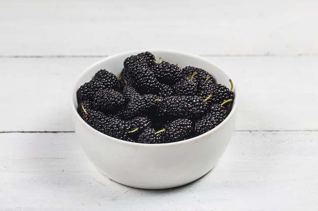 Mulberry fruit in white bowl on wood table