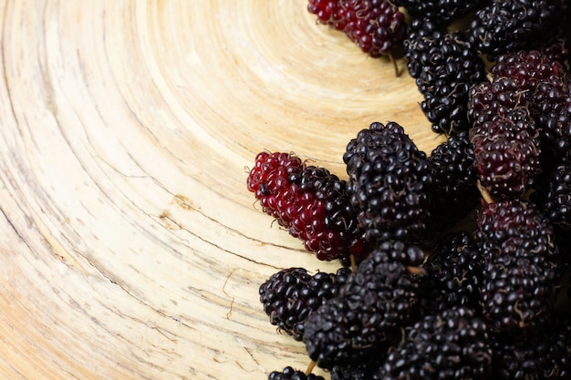 The mulberry fruit in white bowl on wood table.