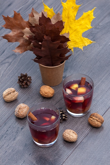 Mulled red wine with spices and fruits on a wooden table. Autumn fall leaves.