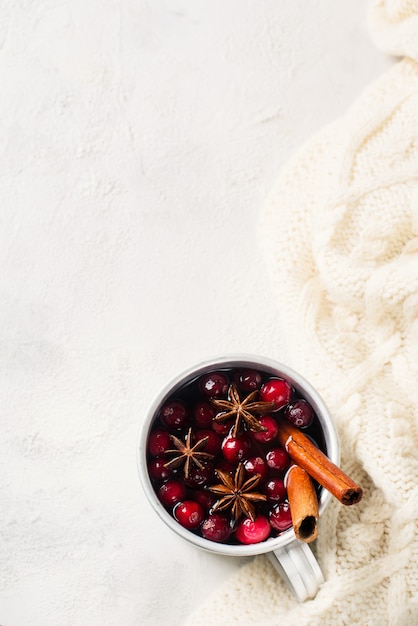 Mulled wine in cup with cranberry and spices on white sweater background