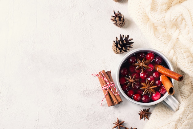 Mulled wine in cup with cranberry and spices on white sweater background