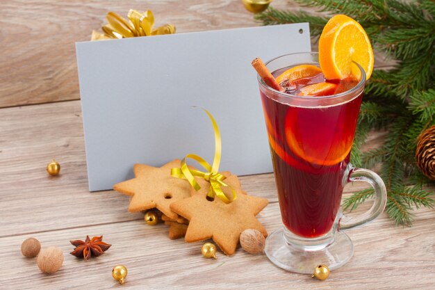 Mulled wine and gingerbread cookies with empty greeting card on wooden table