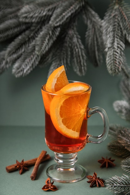 Mulled wine in glass glasses decorated with cinnamon sticks on green christmas tree background